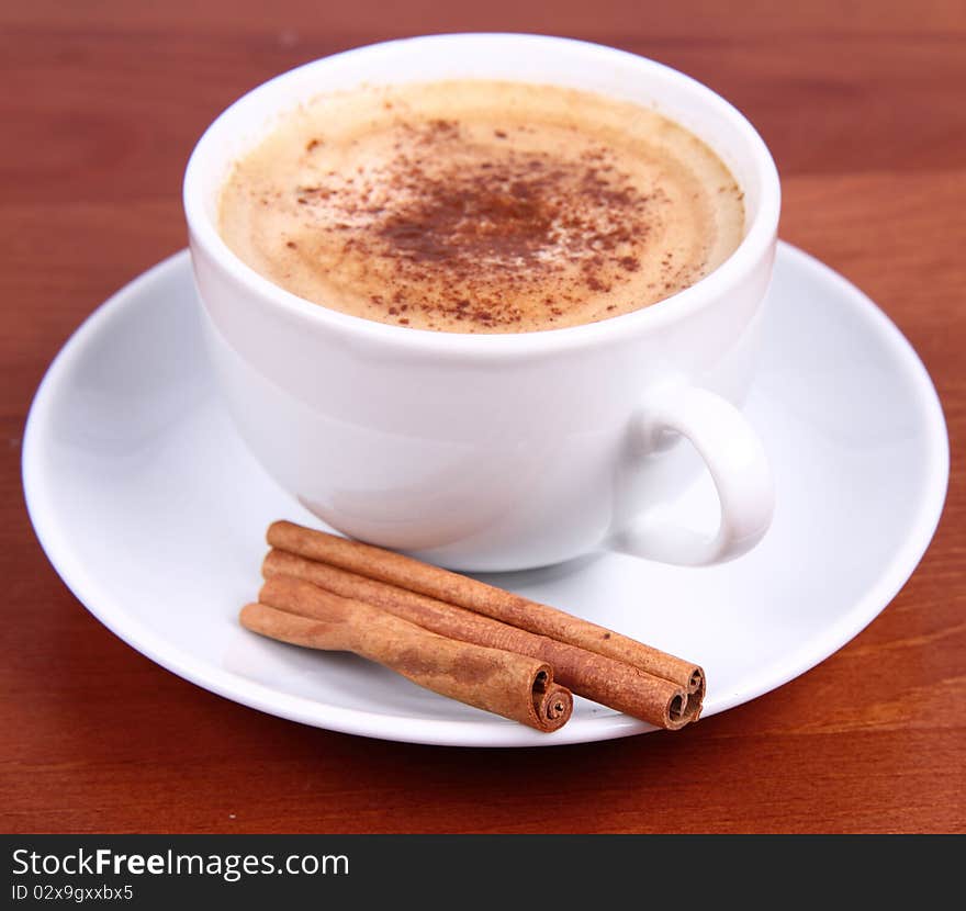 Cup of coffee sprinkled with cinnamon and with cinnamon sticks on wooden background