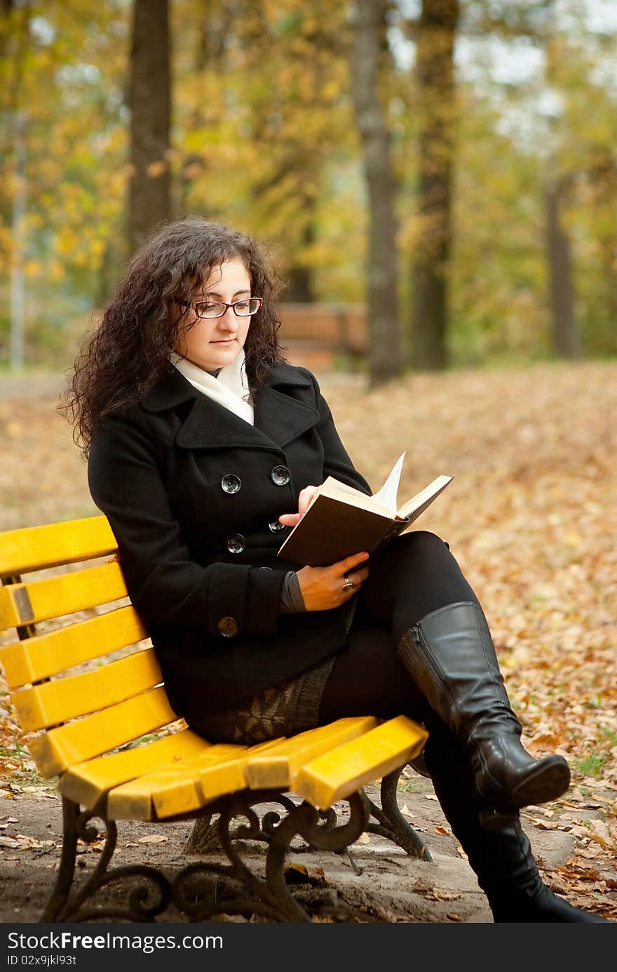 Young Woman Reading Book On Bench