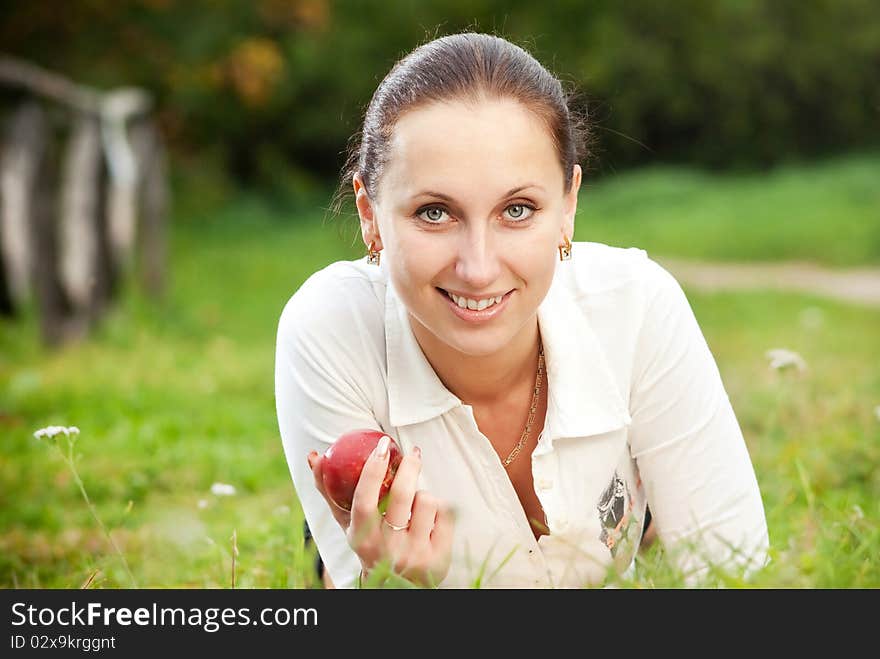 Young woman smilling with apple on grass