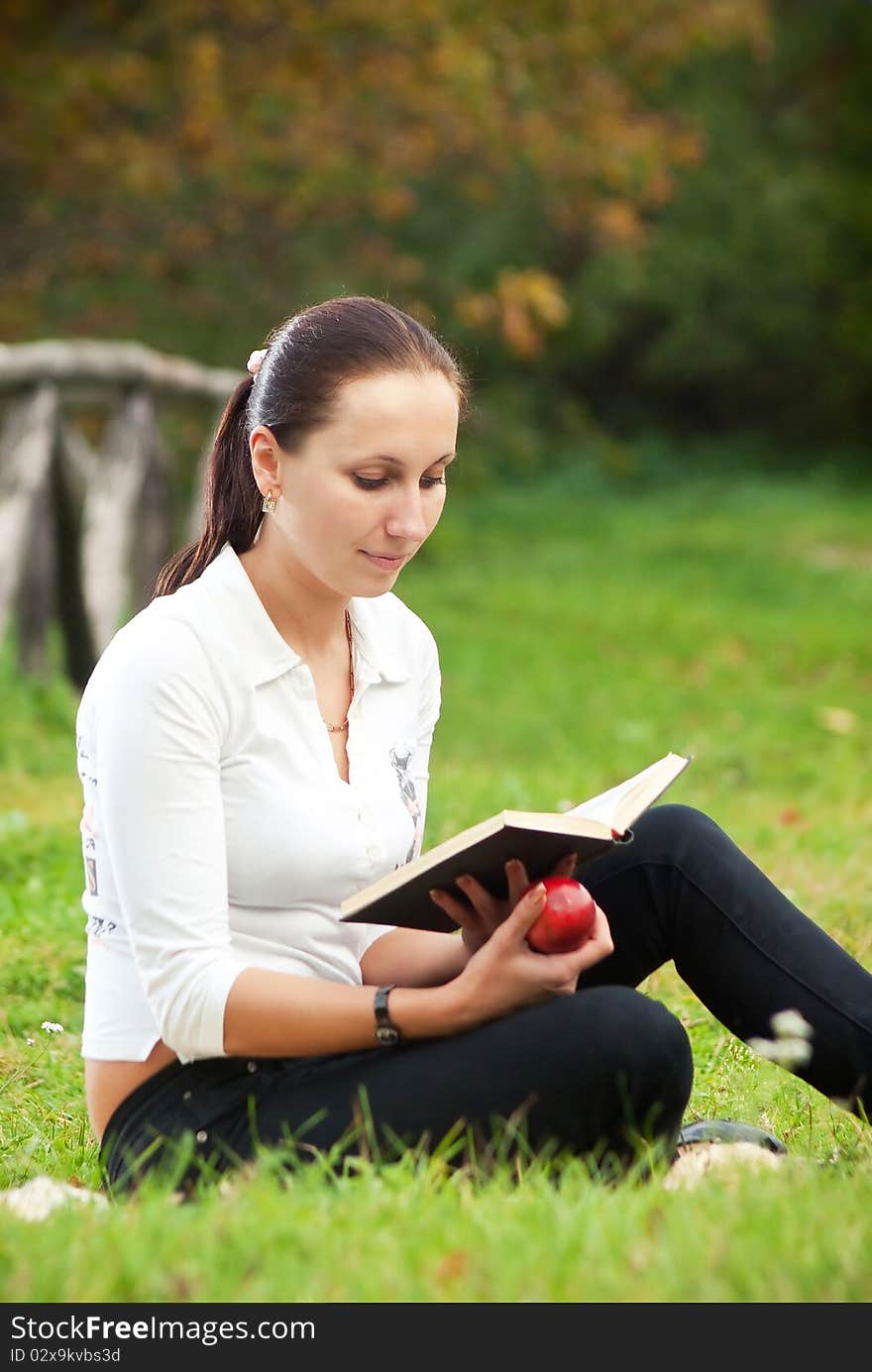 Young woman sitting on grass and reading book