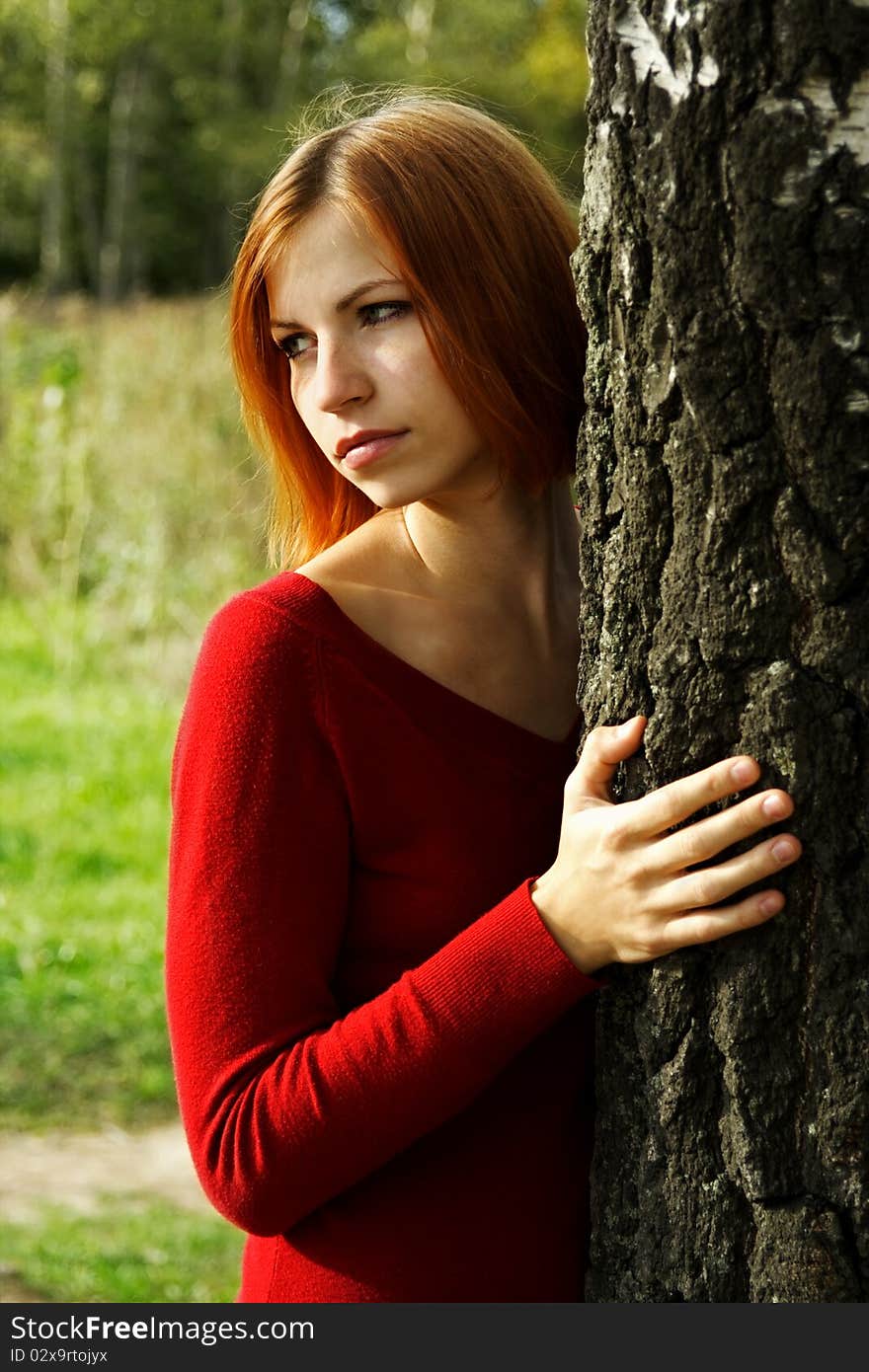 Beauty girl in red dress snuggle up to tree, half body, looking at side