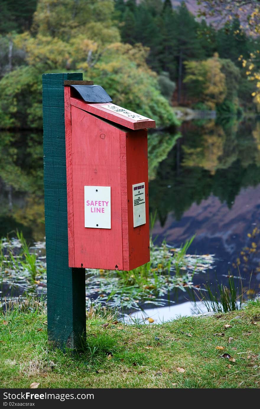 A vertical image of a safety line box beside a loch with autumn reflections