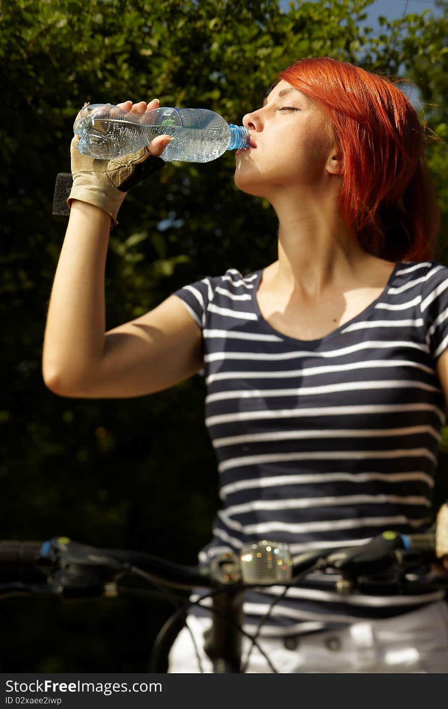 Adult smiling biker woman on mounting bike drinking mineral water. Adult smiling biker woman on mounting bike drinking mineral water