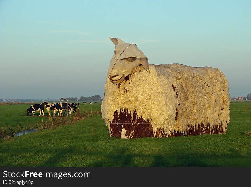 Giant sheep statue in the afternoon sun, with a cows in the background, photo taken in the Netherlands. Giant sheep statue in the afternoon sun, with a cows in the background, photo taken in the Netherlands