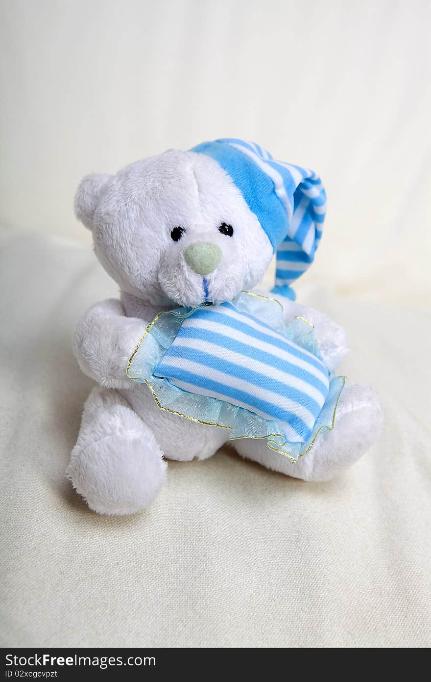 White toy teddy bear with small blue pillow and blue hat. White toy teddy bear with small blue pillow and blue hat