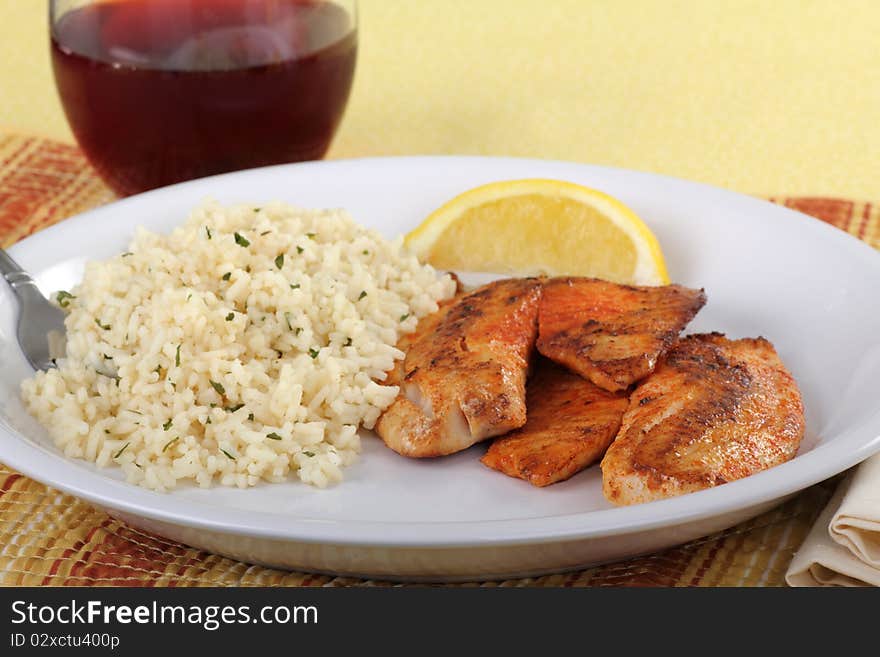 Tilapia fish fillets dinner with with rice, a lemon slice and a drink. Tilapia fish fillets dinner with with rice, a lemon slice and a drink