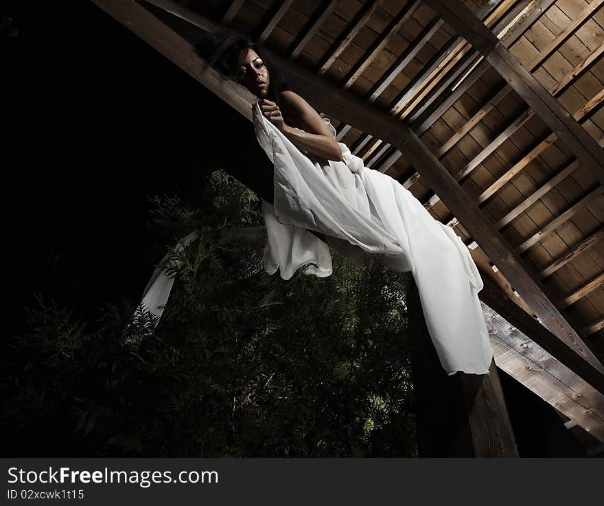 Attractive suntanned girl in white dress poses on a wooden beam. Attractive suntanned girl in white dress poses on a wooden beam.