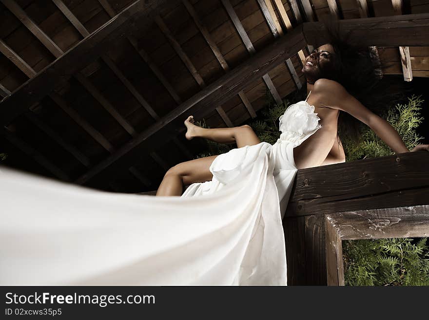 Attractive suntanned girl in white dress poses on a wooden beam. Attractive suntanned girl in white dress poses on a wooden beam.