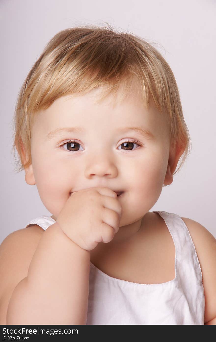 Portrait of happy smiling pretty baby holding finger in mouth, studio shot