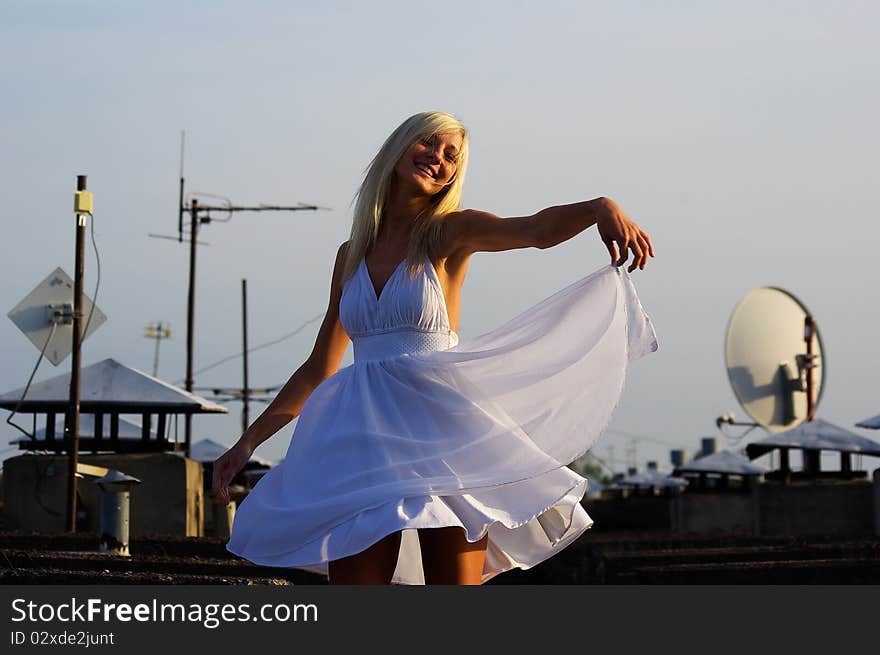 Pretty girl is posing on the roof with white beautiful dress. She is dancing because she likes the good weather. Pretty girl is posing on the roof with white beautiful dress. She is dancing because she likes the good weather.