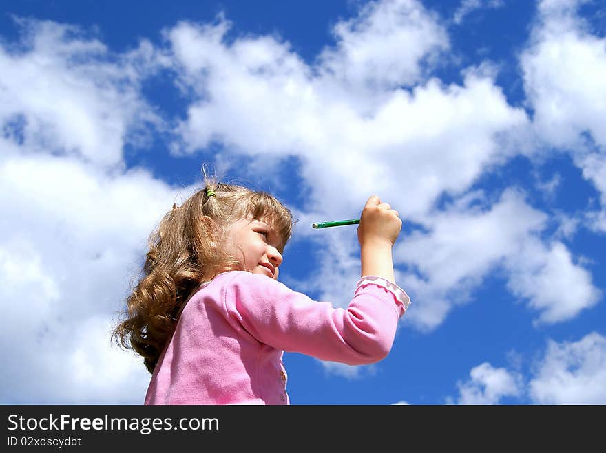 The girl draws a green pencil in the blue sky with white clouds in the summer. The girl draws a green pencil in the blue sky with white clouds in the summer