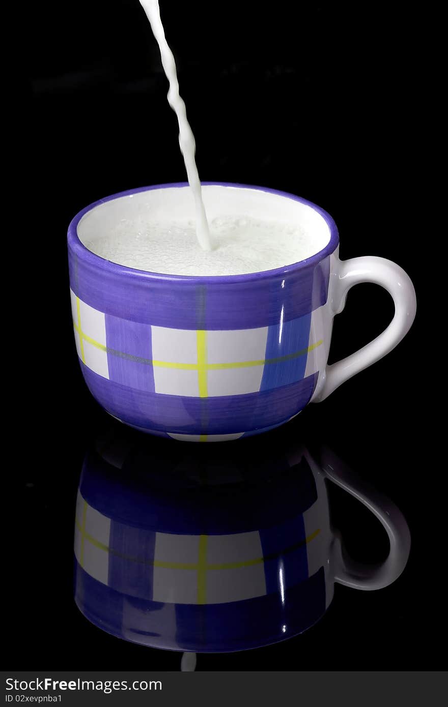 Fresh milk with foam being poured to the blue and white cup on the black backgraund. Fresh milk with foam being poured to the blue and white cup on the black backgraund