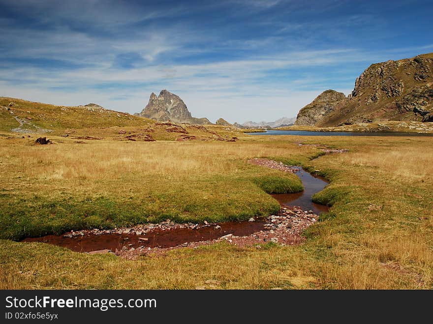 Panorama of Anayet plateau with a small stream red from rocks in Spanich Aragon and Peak du Midi d'Ossau in French Bearn in Pyrenees mountains at background,  in summer time. Panorama of Anayet plateau with a small stream red from rocks in Spanich Aragon and Peak du Midi d'Ossau in French Bearn in Pyrenees mountains at background,  in summer time