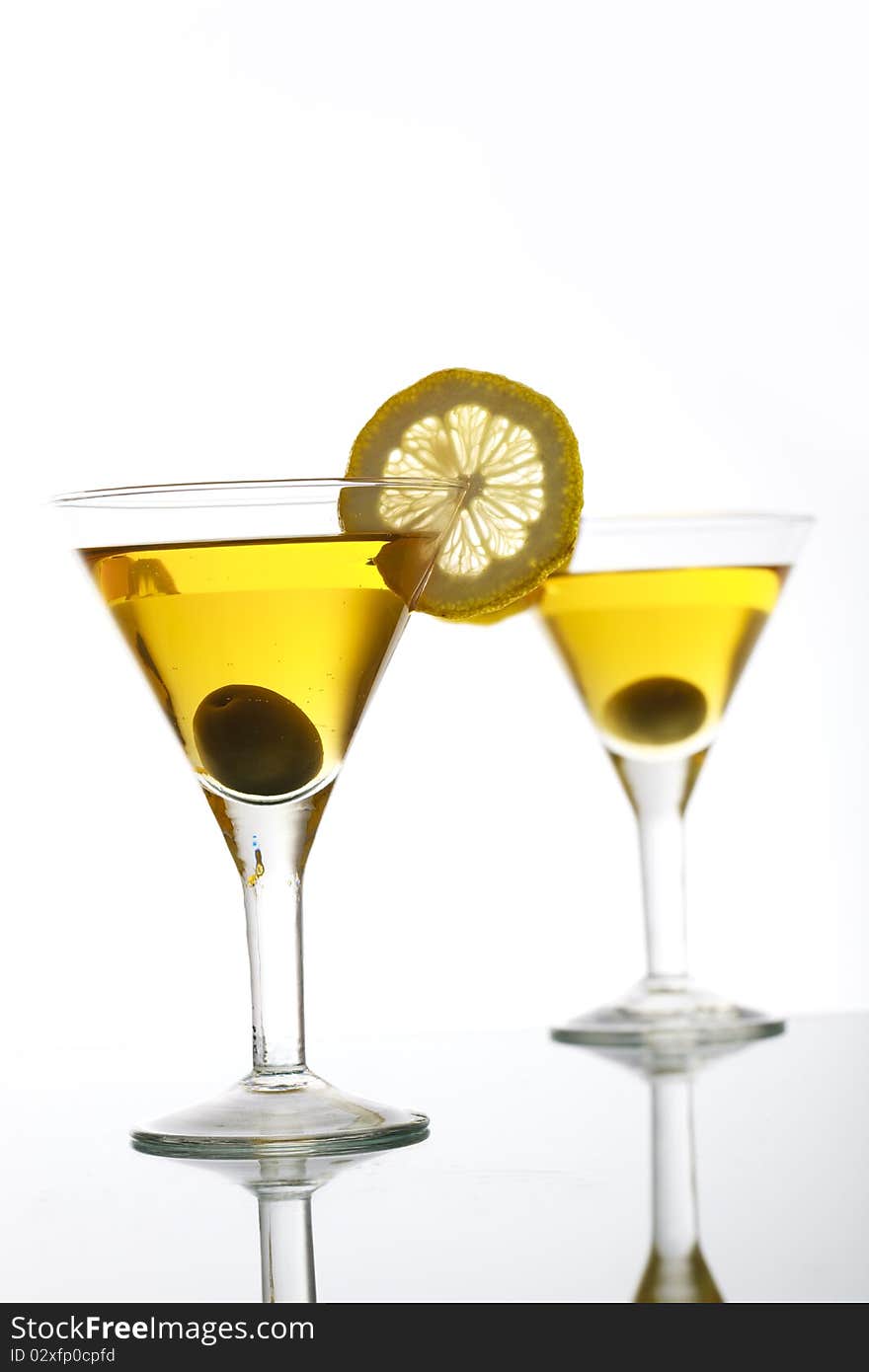 Two glasses with classical martini on reflection surface, garnished olive and lemon. Two glasses with classical martini on reflection surface, garnished olive and lemon.