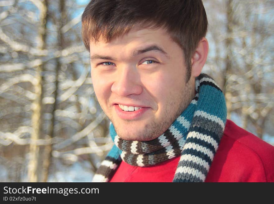 Young funny man in scarf smiling in winter forest