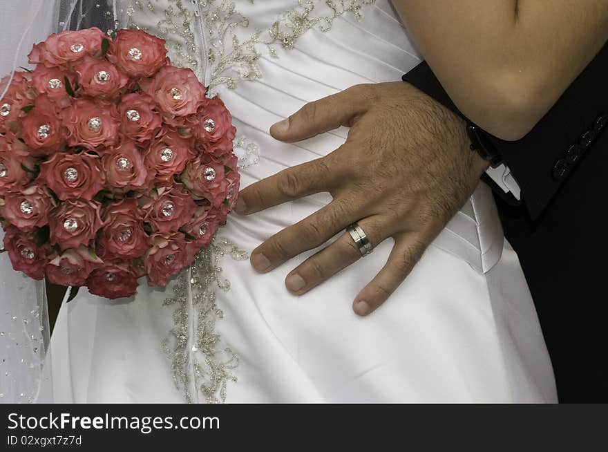 Groom with his hand and red bouquet on his bride