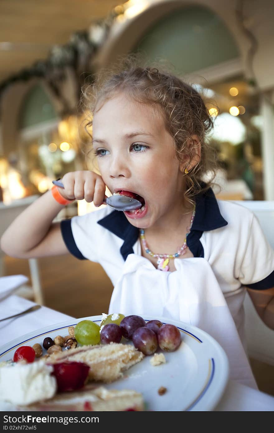 Cute little girl with curly hair eats a cake at the restaurant with widely open mouth. Cute little girl with curly hair eats a cake at the restaurant with widely open mouth