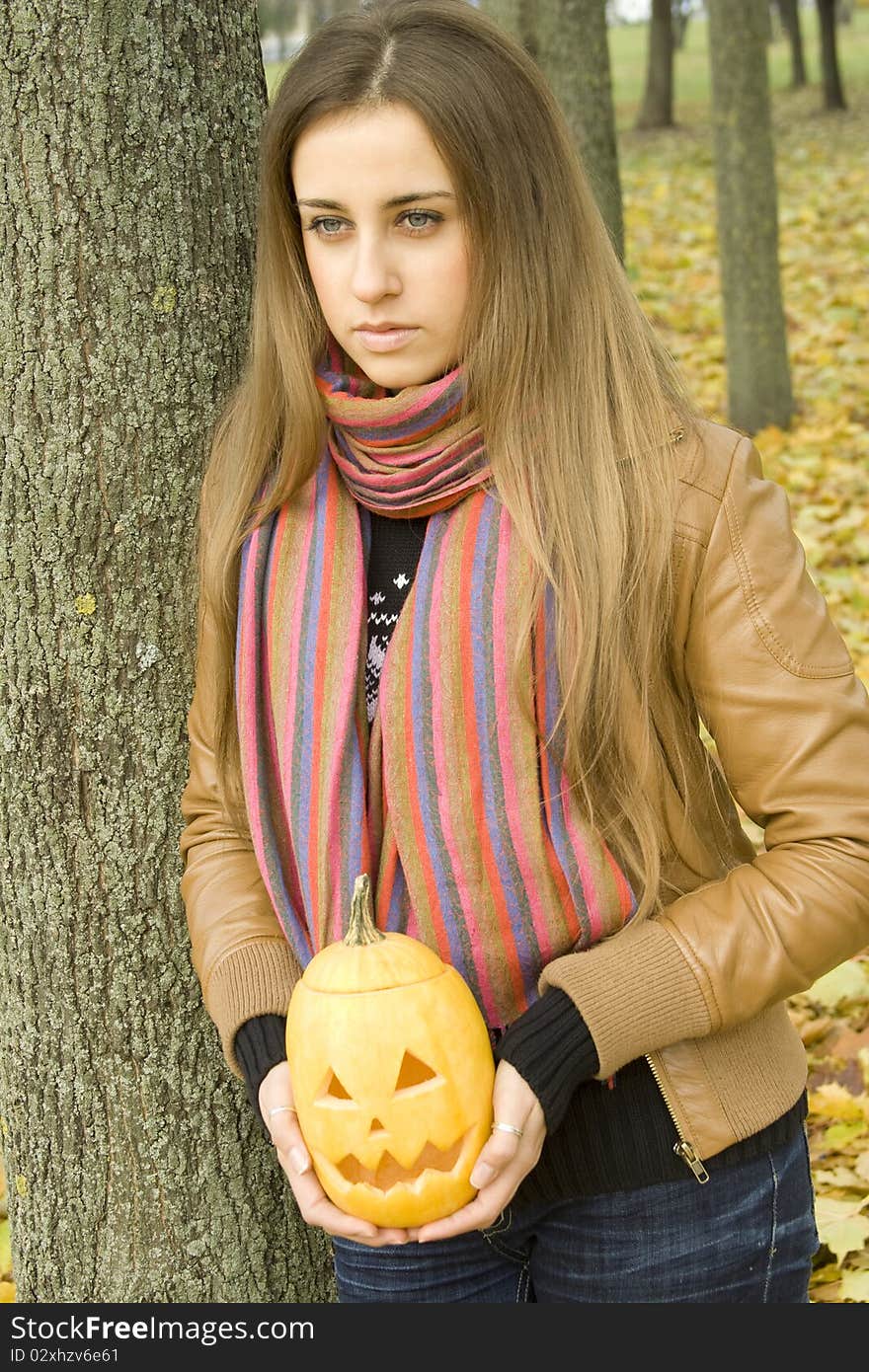 Young girl outdoors in autumn in the park with a pumpkin for Halloween