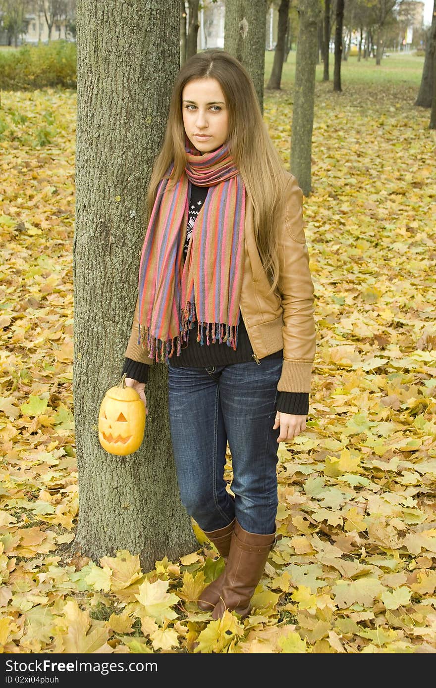 Young girl outdoors in autumn in the park with a pumpkin for Halloween