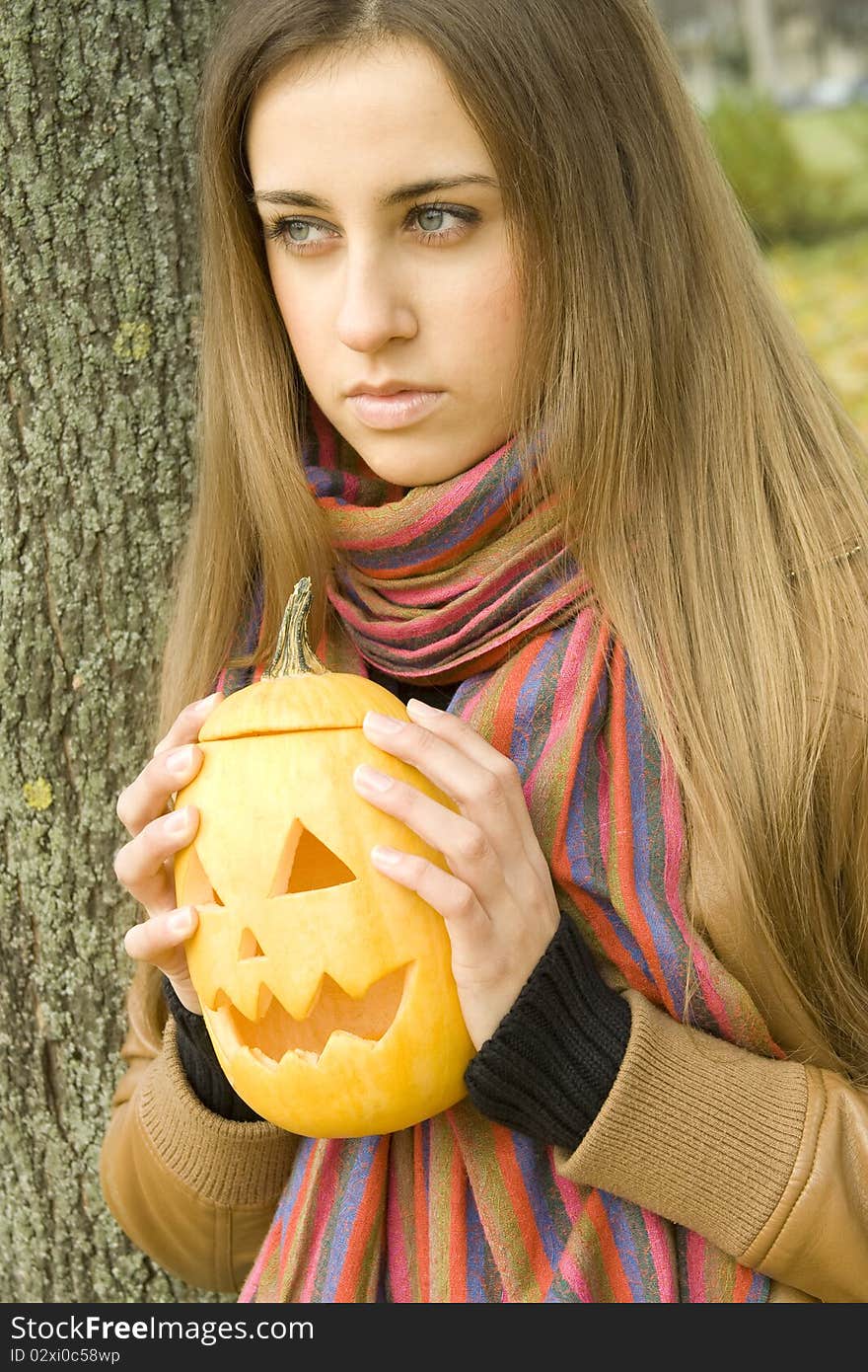 Young girl outdoors in autumn in the park with a pumpkin for Halloween