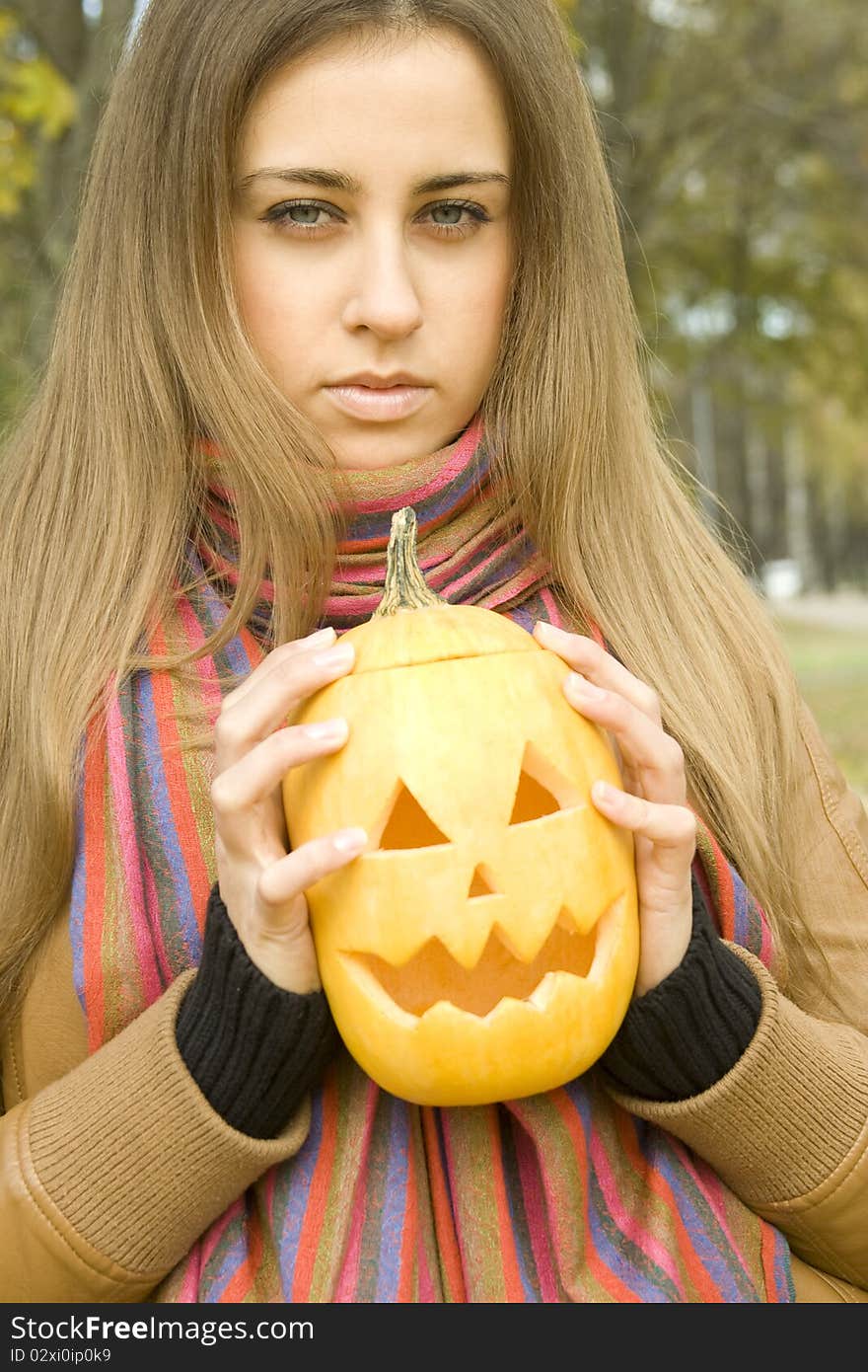 Young girl outdoors in autumn in the park with a pumpkin for Halloween