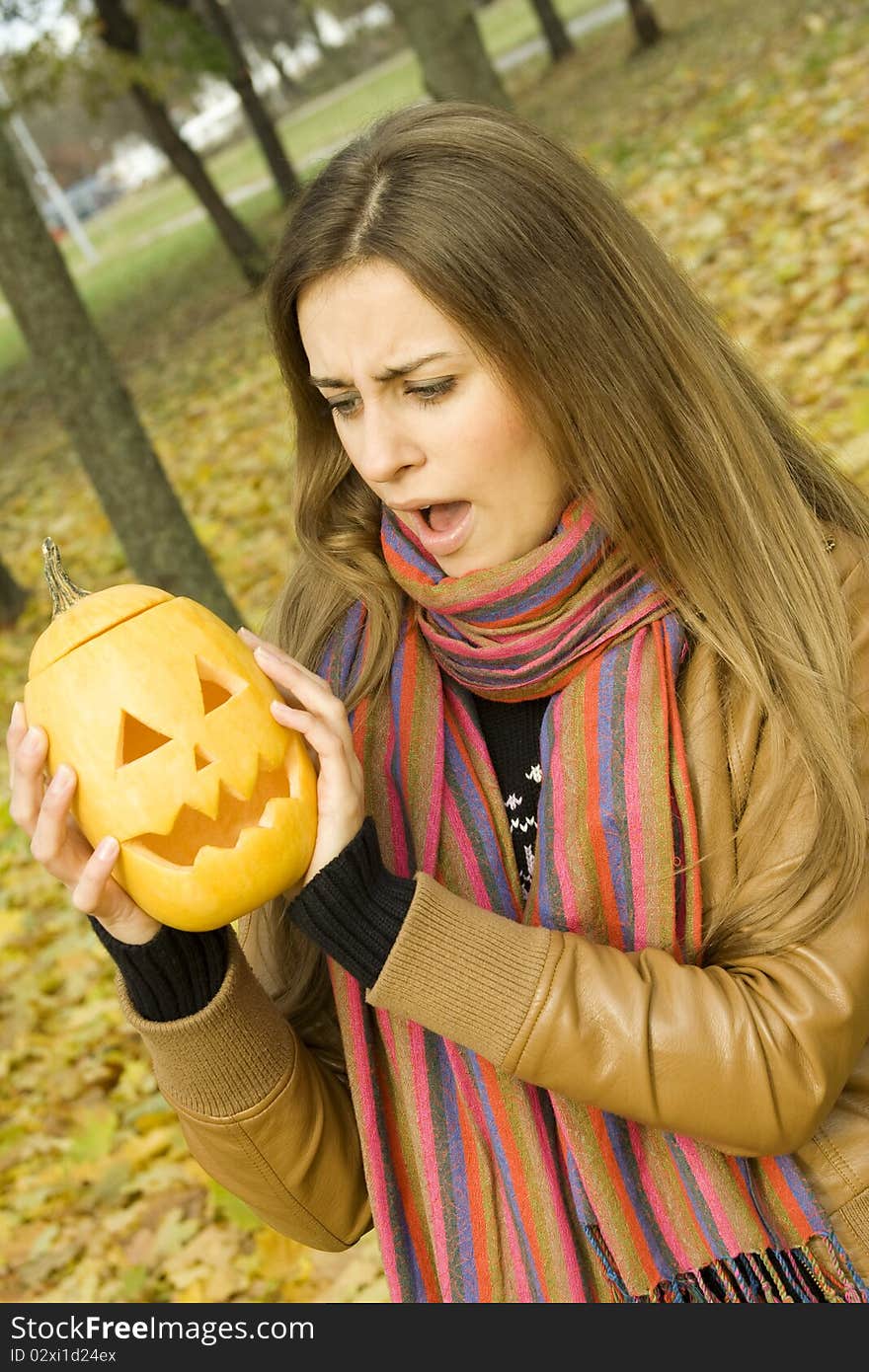 Young girl outdoors in autumn in the park with a pumpkin for Halloween