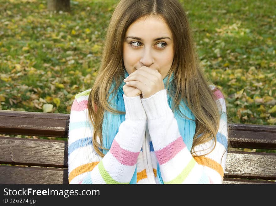 Vertical portrait of a beautiful young woman sitting on a bench in the park around a lot of yellow, red green leaves. Breath warms your hands. Vertical portrait of a beautiful young woman sitting on a bench in the park around a lot of yellow, red green leaves. Breath warms your hands