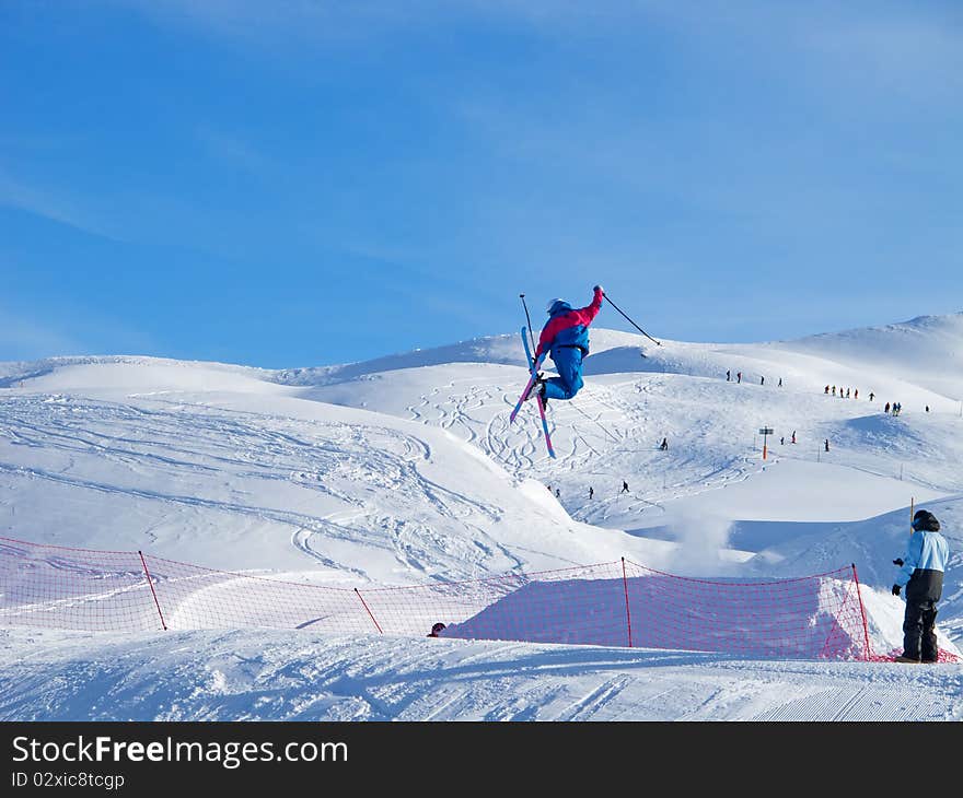 Young skier in blue performing a tele-heli jump