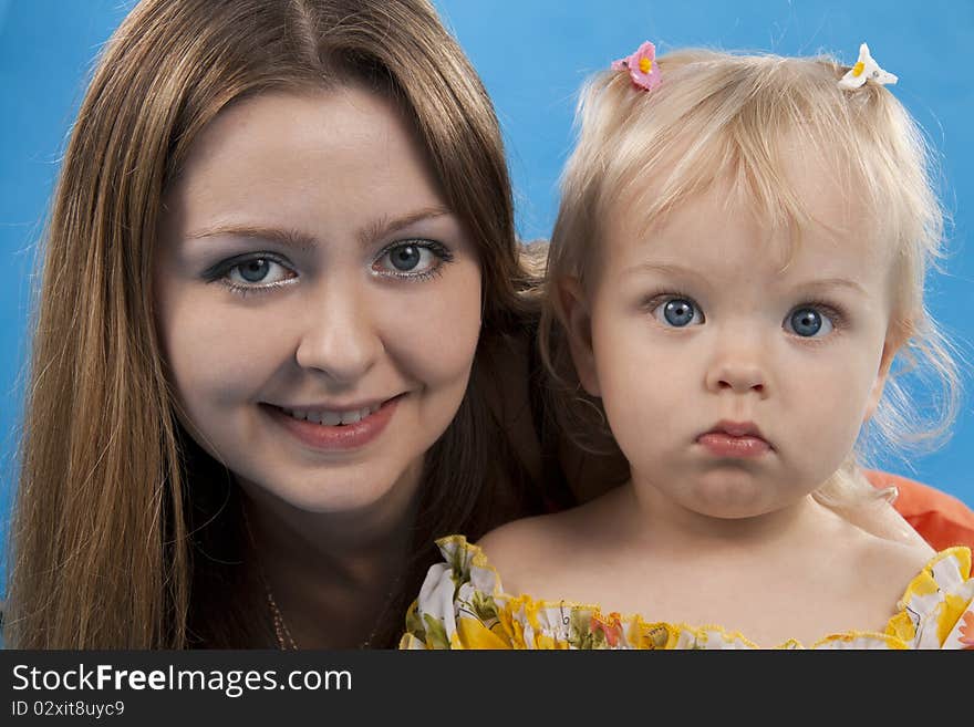 Young and beautiful mother with her sweet little daughter isolated on blue. Young and beautiful mother with her sweet little daughter isolated on blue.