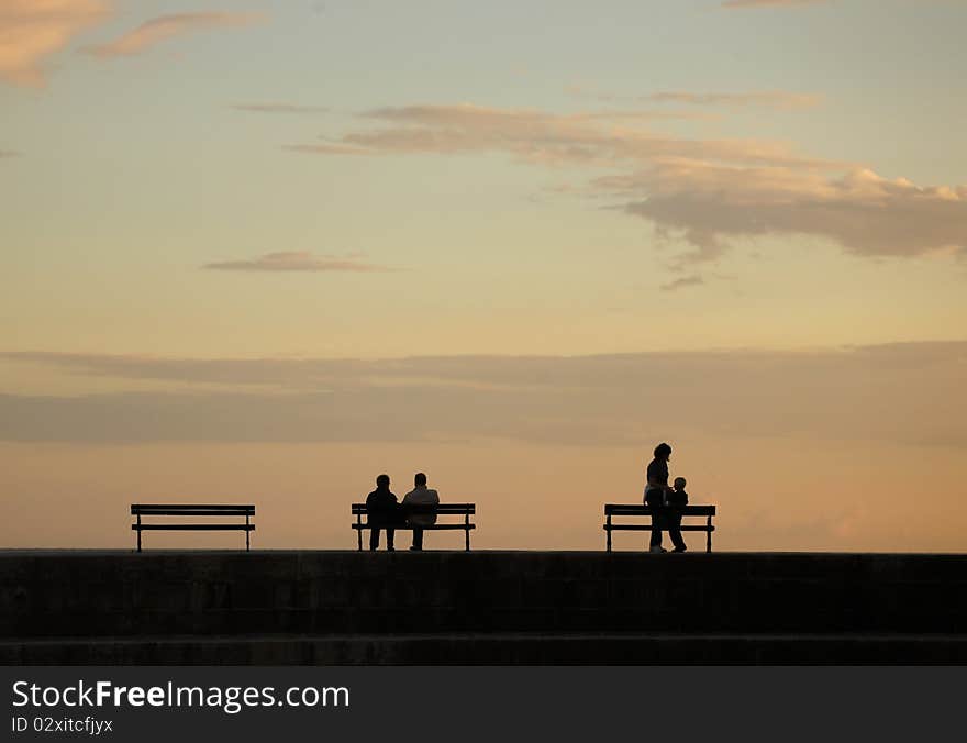 Silhouettes over sunset - pair on one bench and mother with child near another