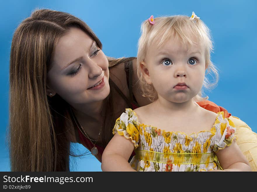 Young and beautiful mother with her sweet little daughter isolated on blue. Young and beautiful mother with her sweet little daughter isolated on blue.