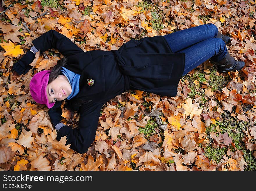 Pretty autumn girl relaxing outdoors in the forest on the fallen leafs