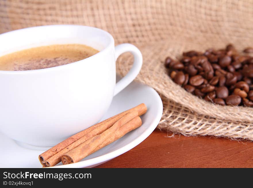 Cup of coffee sprinkled with cinnamon and with cinnamon sticks, coffee beans and burlap material. Cup of coffee sprinkled with cinnamon and with cinnamon sticks, coffee beans and burlap material