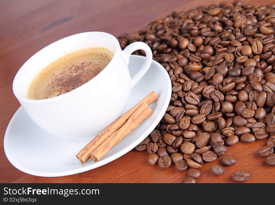 Cup of coffee sprinkled with cinnamon and with cinnamon sticks and coffee beans on a wooden table