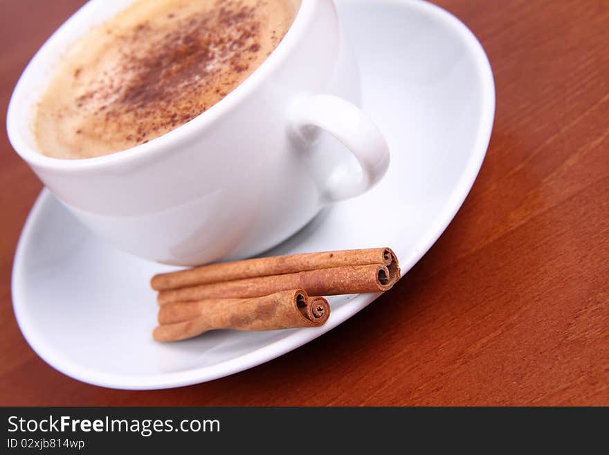 Cup of coffee sprinkled with cinnamon and with cinnamon sticks on wooden background