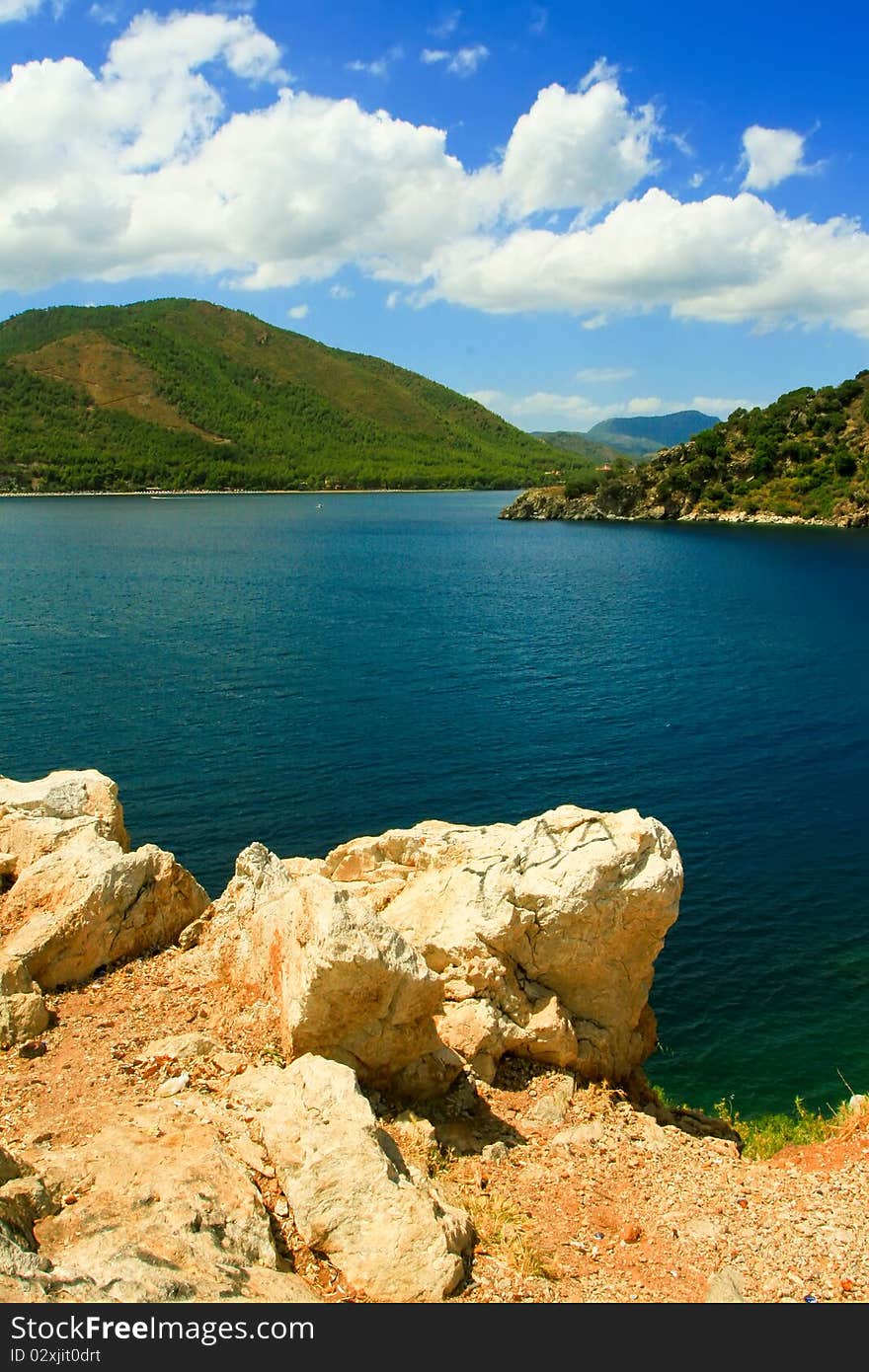 Clear day. Resort. Stones in the foreground, sea expanse and the mountains in the distance. Clear day. Resort. Stones in the foreground, sea expanse and the mountains in the distance