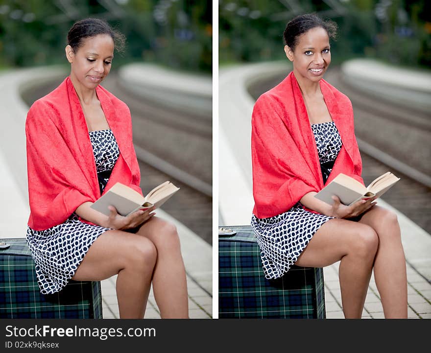 A young lady sitting on her suitcase and reading. A young lady sitting on her suitcase and reading