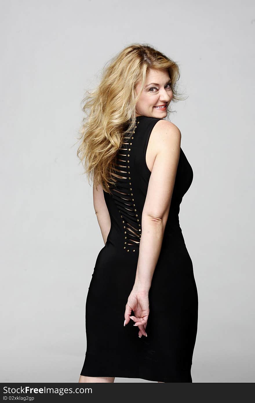 A blond model wearing a black evening dress with ear rings smiles while posing for pictures in studio. A blond model wearing a black evening dress with ear rings smiles while posing for pictures in studio