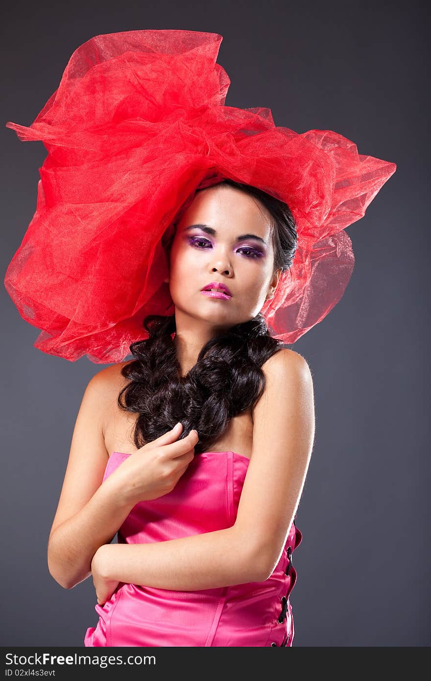 Dreaming beautiful brunette woman in red tulle hat embracing herself