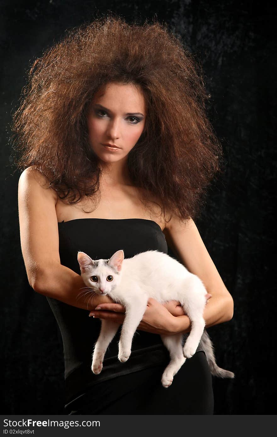 Portrait of the beautiful young woman with a magnificent hairdress And the WHITE CAT ON the SHOULDER on a black background.