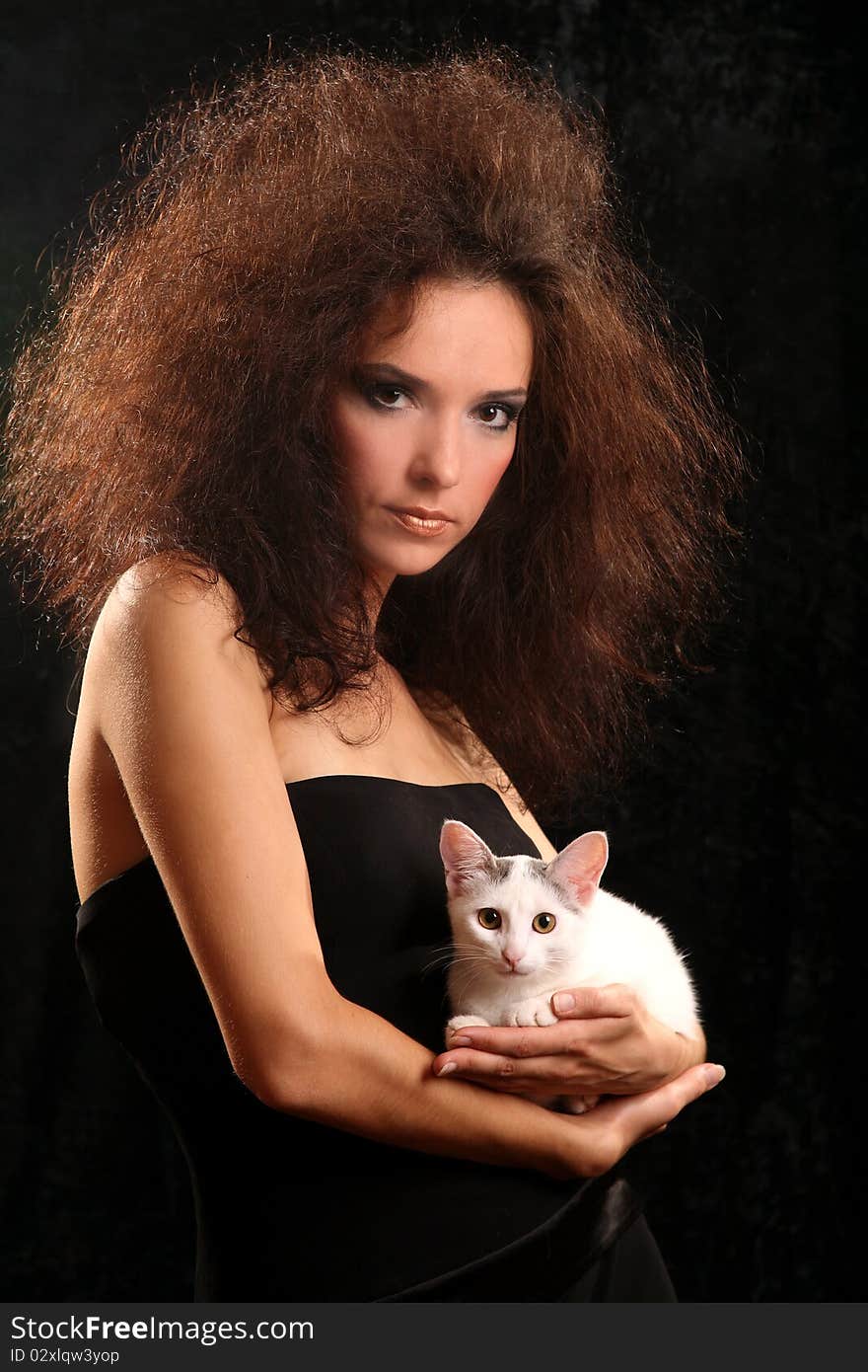 Portrait of the beautiful young woman with a magnificent hairdress And the WHITE CAT ON the SHOULDER on a black background.