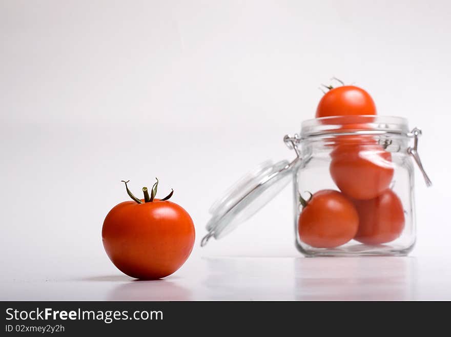 A lonely tomato looking at jar full of tomatoes