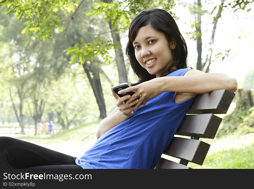 A smiling Asian woman using her cellphone on a park bench. A smiling Asian woman using her cellphone on a park bench