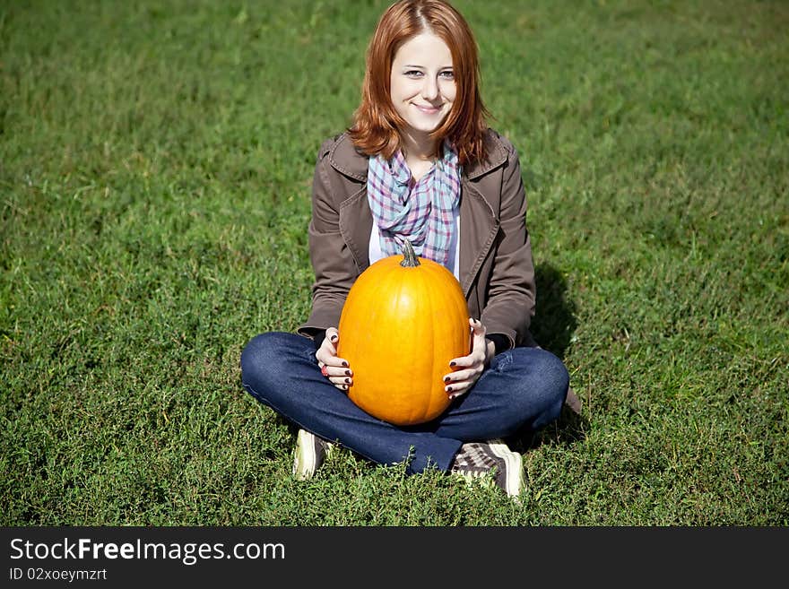 Woman sitting at green grass and keeping pumpkin.