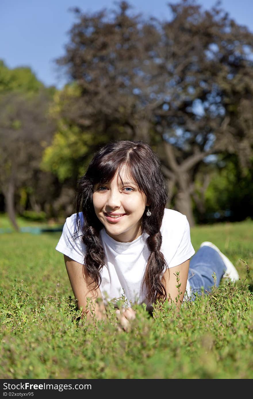 Portrait of beautiful brunette girl with blue eyes on green grass in the park.