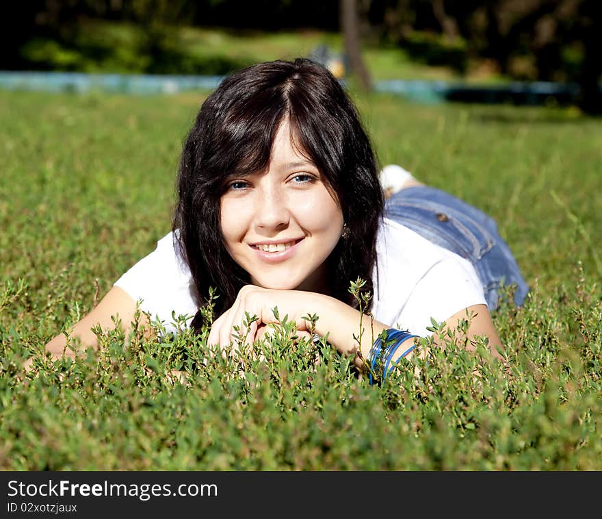 Portrait of beautiful brunette girl with blue eyes on green grass in the park.