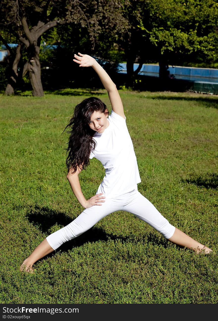 Brunet yoga girl on green grass in park.