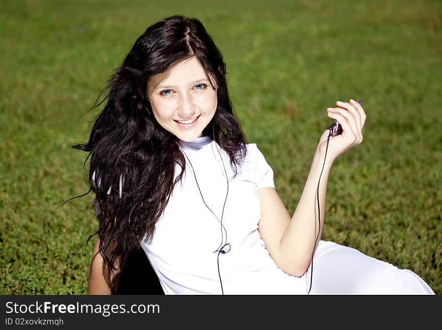 Pretty young brunette girl listening music on green grass in the park and show pink music player. Pretty young brunette girl listening music on green grass in the park and show pink music player.