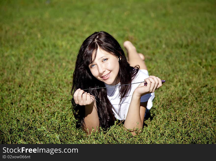 Pretty young brunette girl listening music on green grass in the park and show pink music player. Pretty young brunette girl listening music on green grass in the park and show pink music player.