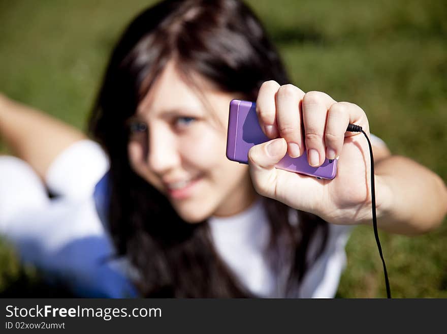 Pretty young brunette girl listening music on green grass in the park and show pink music player. Pretty young brunette girl listening music on green grass in the park and show pink music player.